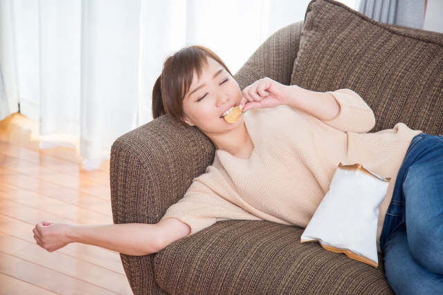 疲労が溜まってソファでくつろぎながらお菓子を食べている女性